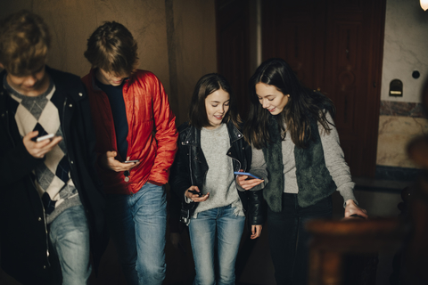 Hohe Winkelansicht von Freunden, die ein Mobiltelefon benutzen, während sie eine Treppe hinaufgehen, lizenzfreies Stockfoto