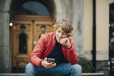 Jugendlicher, der ein Mobiltelefon benutzt, während er auf einer Bank in der Stadt sitzt - MASF00805