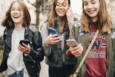 Midsection of female friends using mobile phone while walking in city - MASF00808