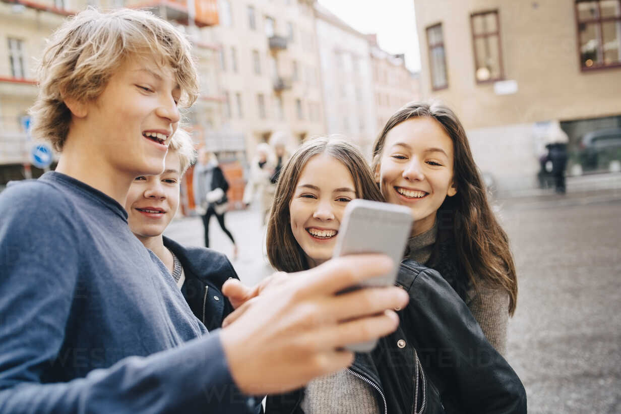 Happy male and female friends looking at mobile phone in city stock photo