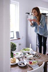 Blogger photographing food at table through mobile phone by window - MASF00829