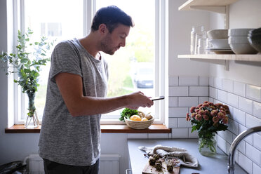 Mid adult man photographing food through smart phone at kitchen counter - MASF00834