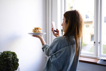 Frau fotografiert Waffeln mit ihrem Smartphone in einem Teller an der Wand zu Hause - MASF00839
