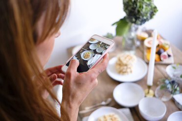 Rear view of woman photographing waffles in plate on table by wall at home - MASF00840