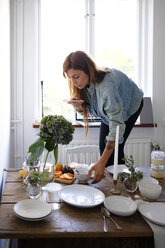Woman photographing plates and food on table at home - MASF00845