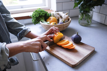 Midsection of woman slicing persimmon on cutting board at kitchen counter - MASF00846