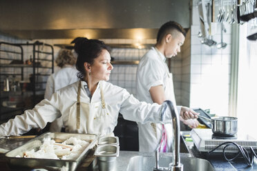 Mature female chef cooking on stove while working in kitchen against colleagues - MASF00867