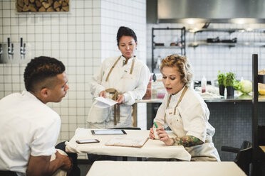 Multi-ethnic owners discussing while sitting at table in restaurant - MASF00879