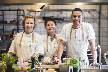 Portrait of smiling confident chefs standing at kitchen in restaurant - MASF00898