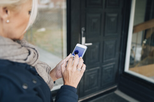 Hochformatige Ansicht einer Frau, die die Haustür über eine Smartphone-App aufschließt - MASF00905