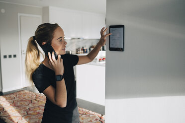 Teenager-Mädchen, das mit einem Smartphone spricht, während es ein digitales Tablet benutzt, das zu Hause an einer weißen Wand angebracht ist - MASF00909