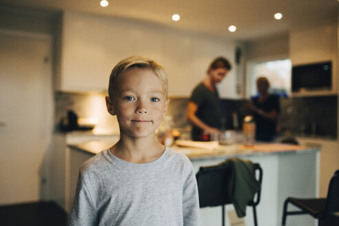 Porträt eines in der Küche stehenden Jungen mit Eltern im Hintergrund - MASF00919