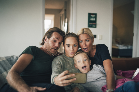 Schockierte Familie, die ein Selfie mit ihrem Smartphone macht, während sie zu Hause auf dem Sofa sitzt, lizenzfreies Stockfoto