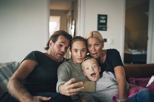 Schockierte Familie, die ein Selfie mit ihrem Smartphone macht, während sie zu Hause auf dem Sofa sitzt - MASF00925
