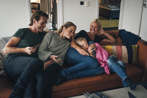 Smiling family looking at boy using mobile phone while sitting on sofa at home stock photo