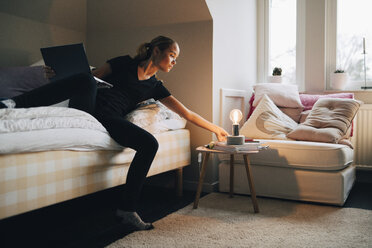 Teenager-Mädchen mit Laptop und Glühbirne in voller Länge im Schlafzimmer zu Hause - MASF00939