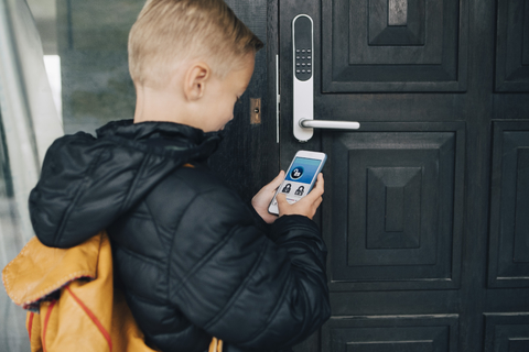 Rear view of boy using app on smart phone to unlock house door stock photo