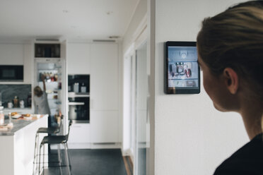 Rückansicht eines Teenagers, der mit einem digitalen Tablet an der Wand steht und seinen Bruder in der Küche betrachtet - MASF00962