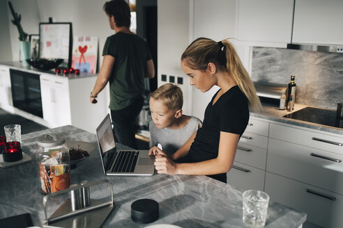 Hoher Blickwinkel des Jungen, der neben seiner Schwester steht und einen Laptop an der Kücheninsel benutzt - MASF00969