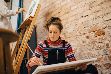 Low angle view of female and male artists painting on canvas at art studio - MASF00977