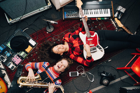 Blick von oben auf glückliche Musikerinnen, die auf einem Teppich liegend Instrumente spielen - MASF00980