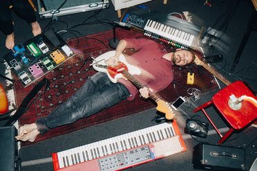Hoher Blickwinkel auf einen Mann, der Gitarre spielt, während er auf einem Teppich im Studio liegt - MASF00982