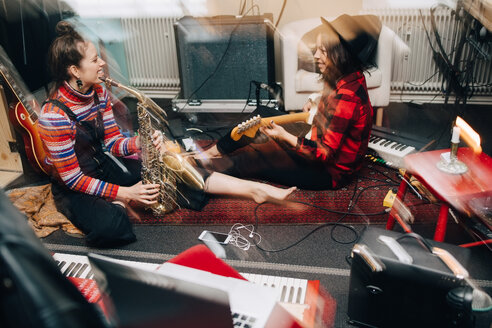 Lächelnde Musikerinnen spielen Instrumente, während sie auf einem Teppich im Studio sitzen - MASF00983