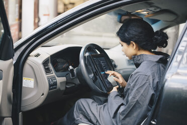 Seitenansicht eines weiblichen Mechanikers, der im Auto sitzend ein digitales Tablet benutzt - MASF00991