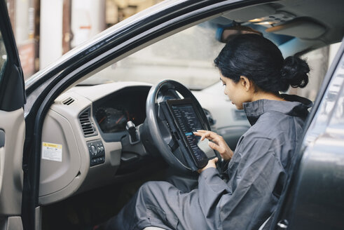Side view of female mechanic using digital tablet while sitting in car - MASF00991