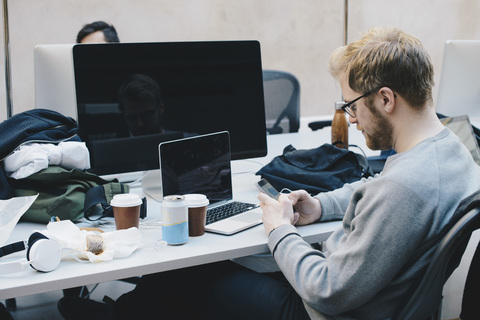 Side view of computer programmer using smart phone at desk in office stock photo