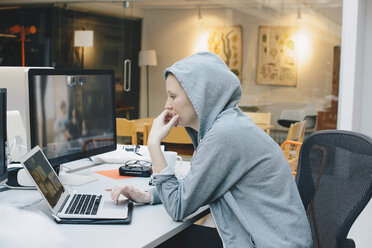 Side view of computer programmer using laptop at desk in office - MASF01003