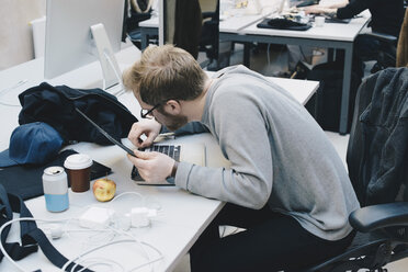 Seitenansicht eines Computerprogrammierers, der ein digitales Tablet an der Tastatur eines Schreibtisches im Büro befestigt - MASF01004