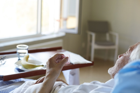 Älterer Mann nimmt Hustensaft ein, während er auf dem Krankenhausbett liegt, lizenzfreies Stockfoto