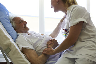 Seitenansicht eines glücklichen älteren Mannes im Gespräch mit einer Krankenschwester auf einem Krankenhausbett - MASF01011
