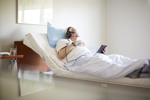 Ein älterer Mann benutzt ein digitales Tablet auf einem Bett in einer Krankenhausabteilung - MASF01017