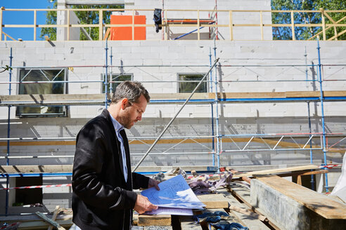 Seitenansicht eines Architekten, der einen Bauplan an einem unvollständigen Gebäude auf einer Baustelle liest - MASF01028