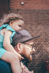 Side view of mid adult man carrying daughter on shoulders against brick wall - MASF01035