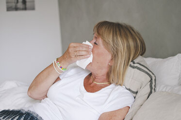 Kranke ältere Frau schnäuzt sich die Nase, während sie zu Hause im Bett liegt - MASF01039