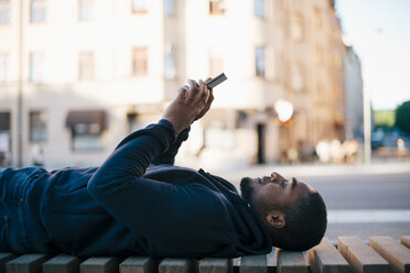 Side view of man lying on bench while using smart phone in city - MASF01041