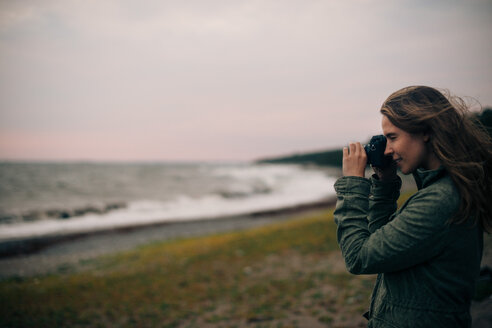 Seitenansicht einer jungen Frau, die das Meer am Strand fotografiert - MASF01051