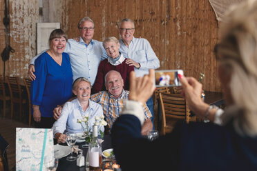 Ältere Frau fotografiert glückliche Freunde, die in einem Restaurant am Tisch sitzen - MASF01069