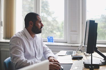 Seitenansicht eines reifen Geschäftsmannes, der einen Computer am Schreibtisch in einem kreativen Büro benutzt - MASF01072