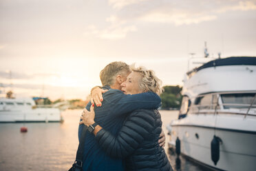 Seitenansicht eines älteren Mannes und einer Frau, die sich am Hafen bei Sonnenuntergang umarmen - MASF01075