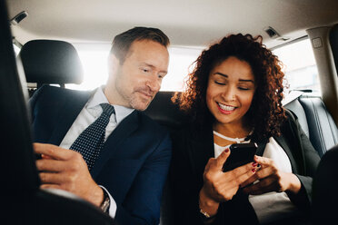 Lächelnde Geschäftsleute teilen sich ein Smartphone, während sie im Taxi sitzen - MASF01102