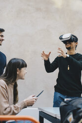 Smiling male computer programmer gesturing while using VR glasses by colleagues in office - MASF01123