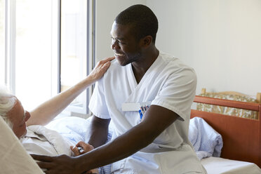 Smiling male nurse consoling senior man in hospital ward - MASF01124
