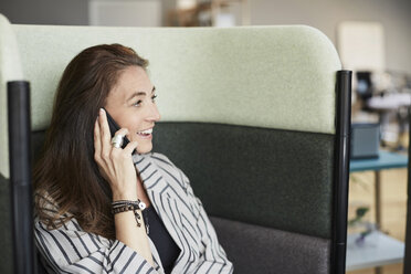 Smiling mature businesswoman talking through mobile phone while sitting on chair at creative office - MASF01129