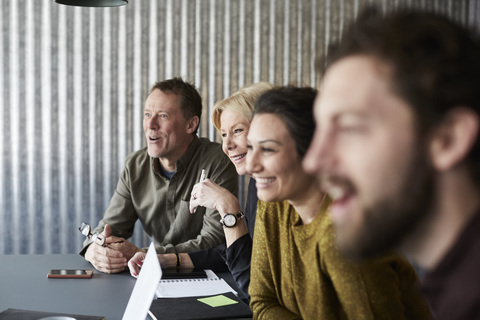 Smiling creative business colleagues sitting at conference table while looking away in board room stock photo