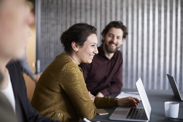 Smiling creative business team sitting with laptop at conference table in board room - MASF01136