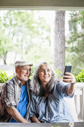 Smiling senior couple taking selfie in porch - MASF01157